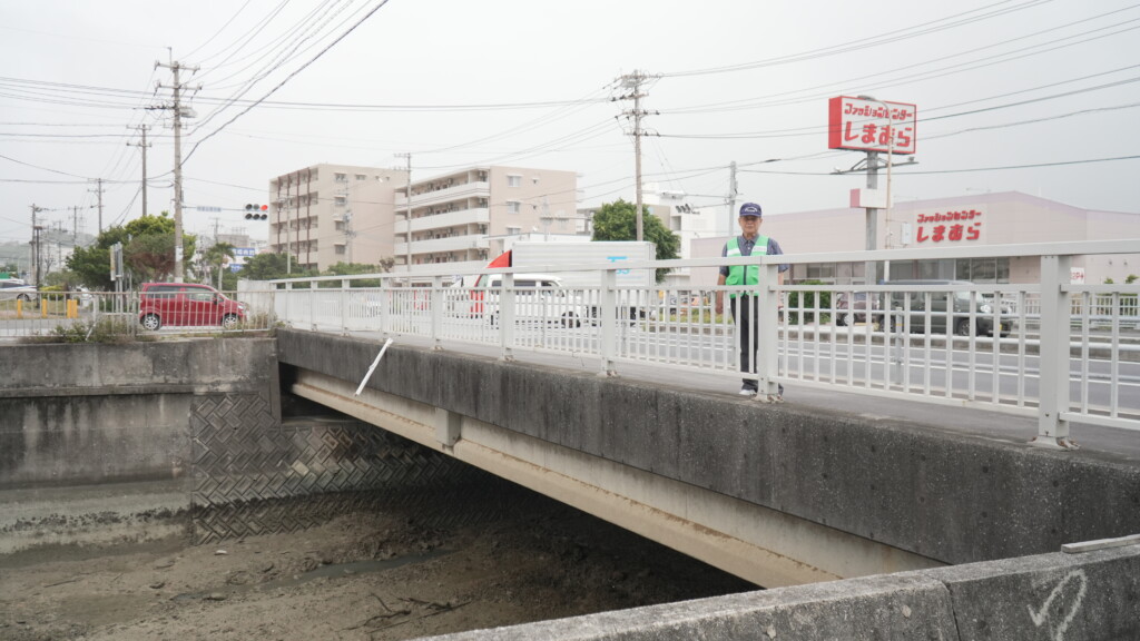 避難経路上の橋に立つ古我知進さん。橋の下には川が流れている。