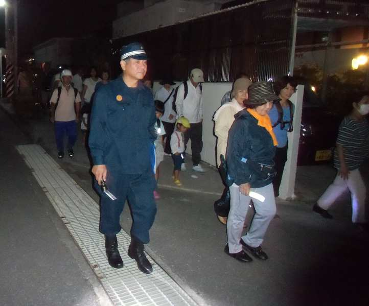 夜間避難訓練の様子。懐中電灯を持った住民たちが暗闇の中を歩いている