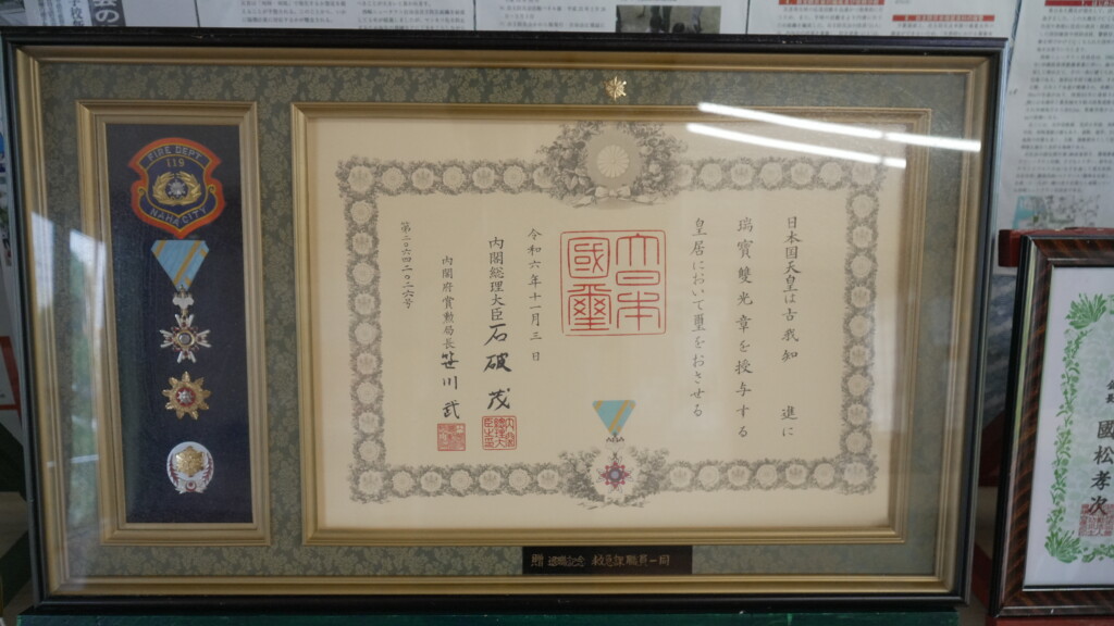 瑞宝双光章の勲記と勲章。那覇市消防局のエンブレムとともに額装されている