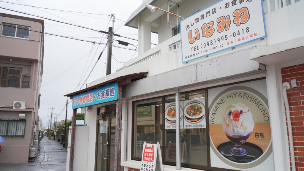 沖縄県糸満市の住宅街に建つ、いなみね冷やしもの店の外観。白い建物に爽やかな水色の看板が掲げられている