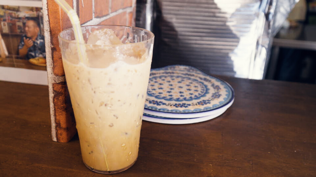 ベトナムカフェオレ。氷が入ったグラスに、練乳入りのコーヒーが注がれている。背景にベトナムの写真が立てかけられている