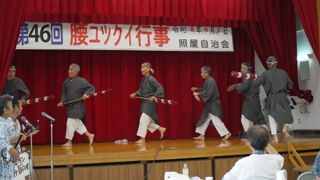 エークを手に群舞するゲキラン十日の会のメンバーと、左で三線を弾く地謡(腰ユックイ行事